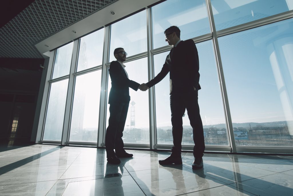 Two,Young,Businessmen,Are,Shaking,Hands,With,Each,Other,Standing